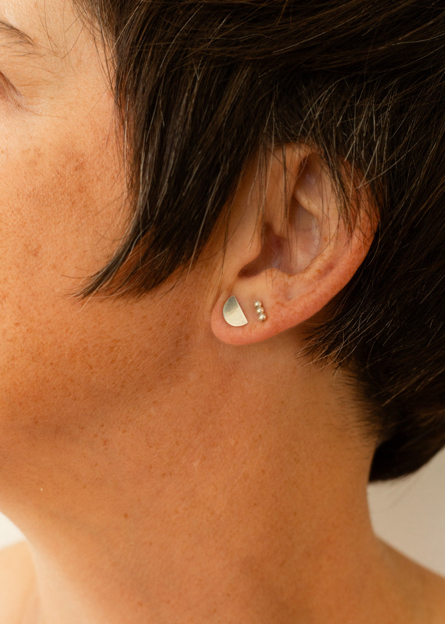 Close-up of model earlobe with a half moon earring and triple ball bar stud