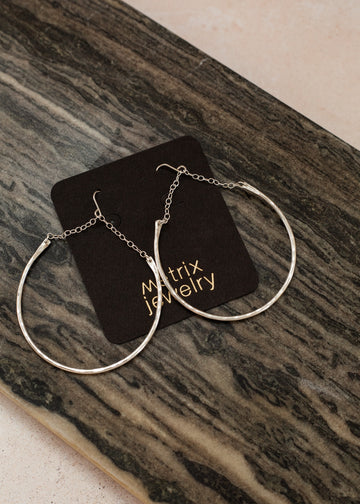 flat-lay of crescent-shaped earring with chain link accents on a black jewelry card and dark wood underneath