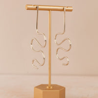 Squiggle statement earrings in sterling silver hanging on a gold earring holder