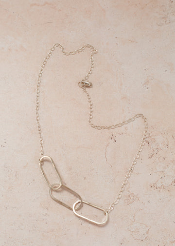 Flat lay of a sterling silver necklace & chain with three oval shaped pieces
