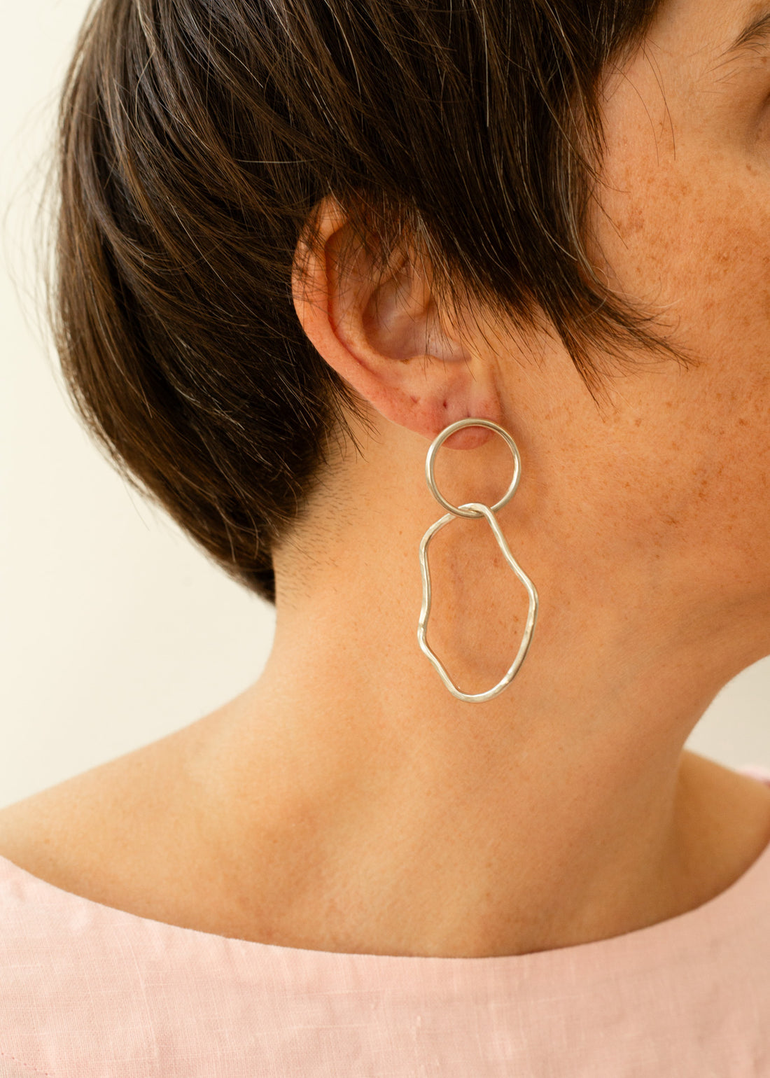 Sterling silver hoop with an organic shape hoop attached, hanging on a model