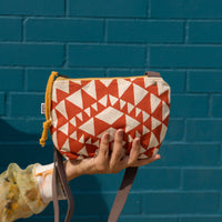 in front of a blue brick wall, a woman holding a crossbody aztec designed bag in her palm