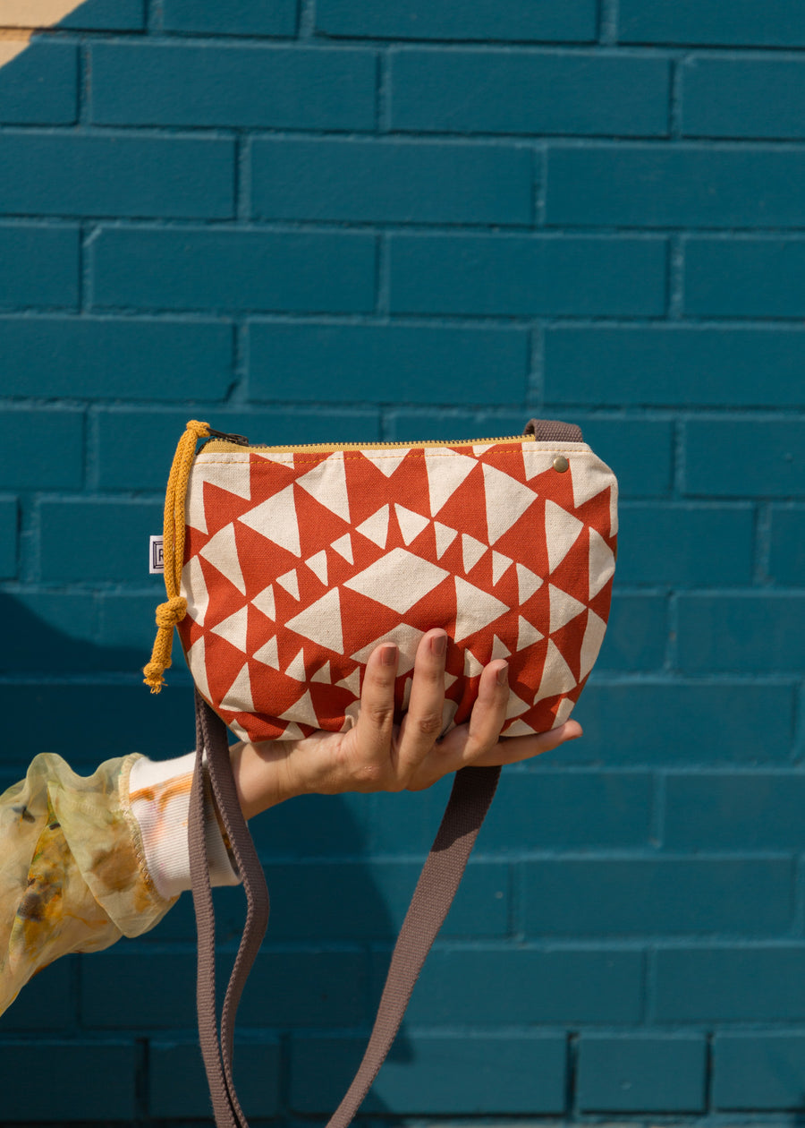 in front of a blue brick wall, a woman holding a crossbody aztec designed bag in her palm