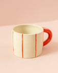 Photo of a cream ceramic mug with light red stripes going around the mug vertically, and a red handle.