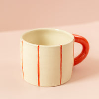 Photo of a cream ceramic mug with light red stripes going around the mug vertically, and a red handle.