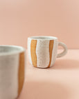 Ceramic mug with white glaze around the mug, with hints of original clay color showing. Another mug is in the foreground