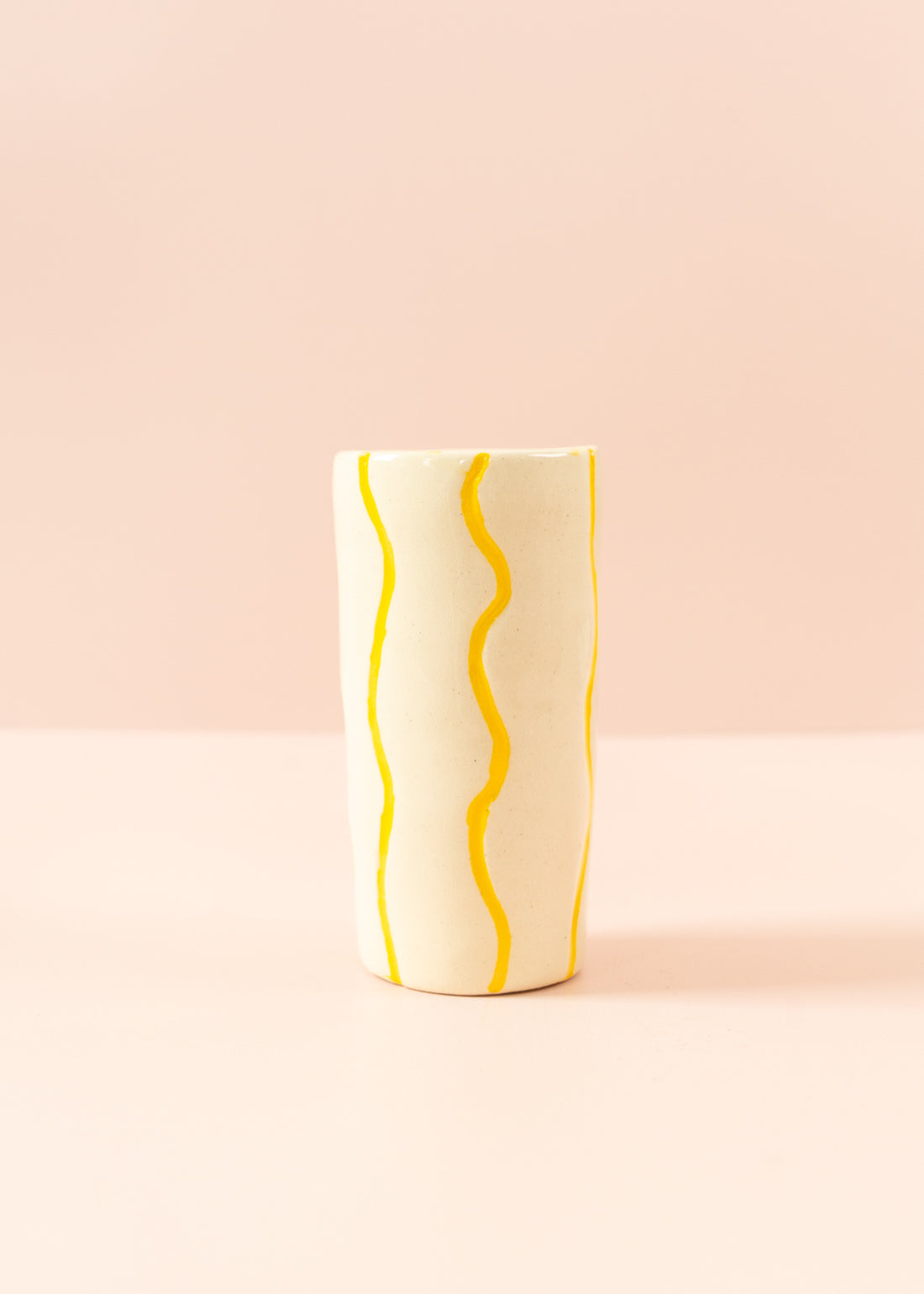 Smal cream vase with squiggly, bright yellow paint lines running vertically around the vase.