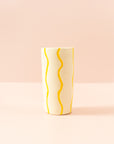 Smal cream vase with squiggly, bright yellow paint lines running vertically around the vase.