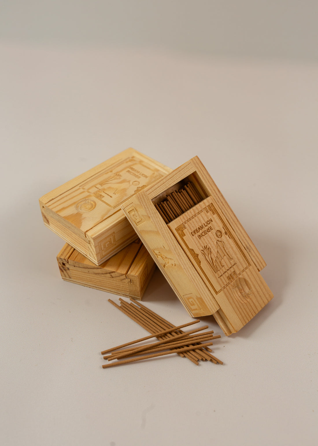 3 wooden boxes piled up with one angles towards the camera and half open to reveal mini incense sticks, with a few piled up in front of the boxes
