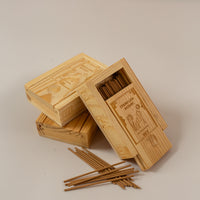 3 wooden boxes piled up with one angles towards the camera and half open to reveal mini incense sticks, with a few piled up in front of the boxes