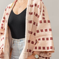Close-up photo of model wearing a pink jacket in the color pink with lines of dark pink square patters all over. Jacket has a mustard yellow color detail, and is 3/4 sleeves