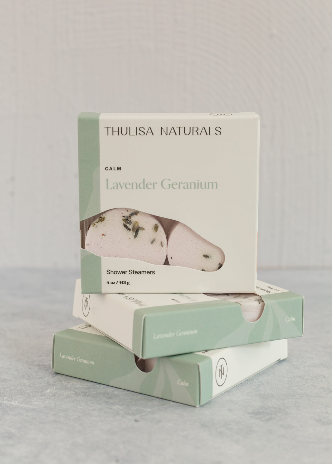 Two boxes of shower steamers with one standing up on top. Boxes are white and green and "lavender geranium" scented