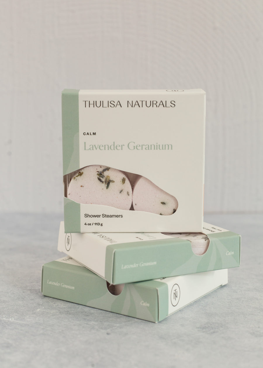 Two boxes of shower steamers with one standing up on top. Boxes are white and green and "lavender geranium" scented