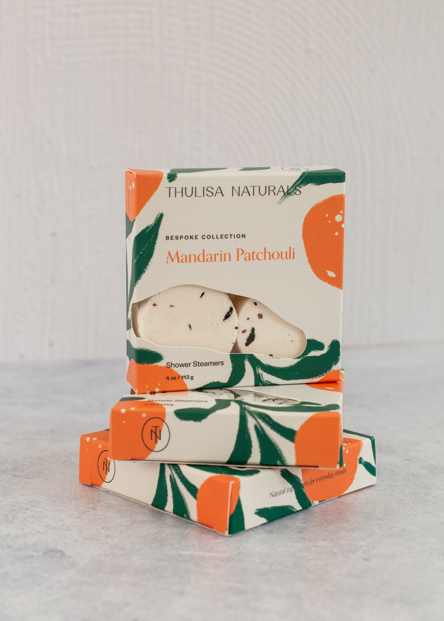 Two boxes of shower steamers with one standing up on top. Boxes are white, orange and green and "Mandarin Patchouli" scented