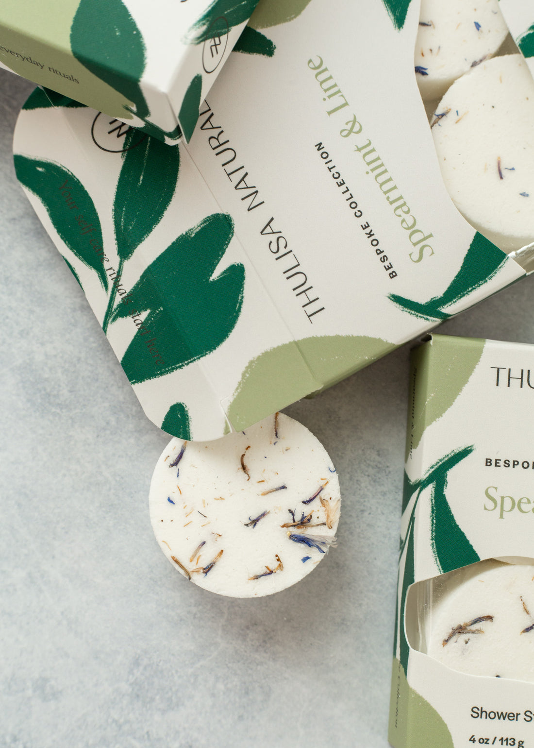 Close-up of a spearmint and lime shower steamer with boxes surrounding