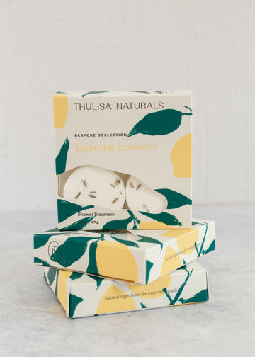 Two boxes of shower steamers with one standing up on top. Boxes are white, yellow and green and "lemon and lavender" scented