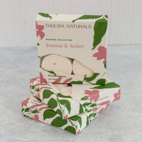 Two boxes of shower steamers with one standing up on top. Boxes are white, pink and green and "jasmine and amber" scented