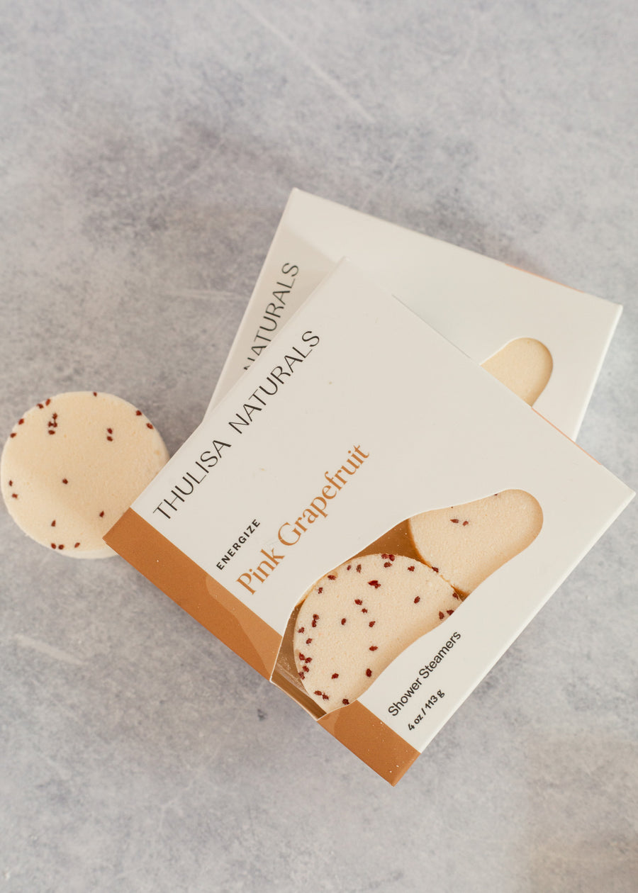 Flatlay of two shower steamer boxes in pink grapefuit scent with a shower steam on the left