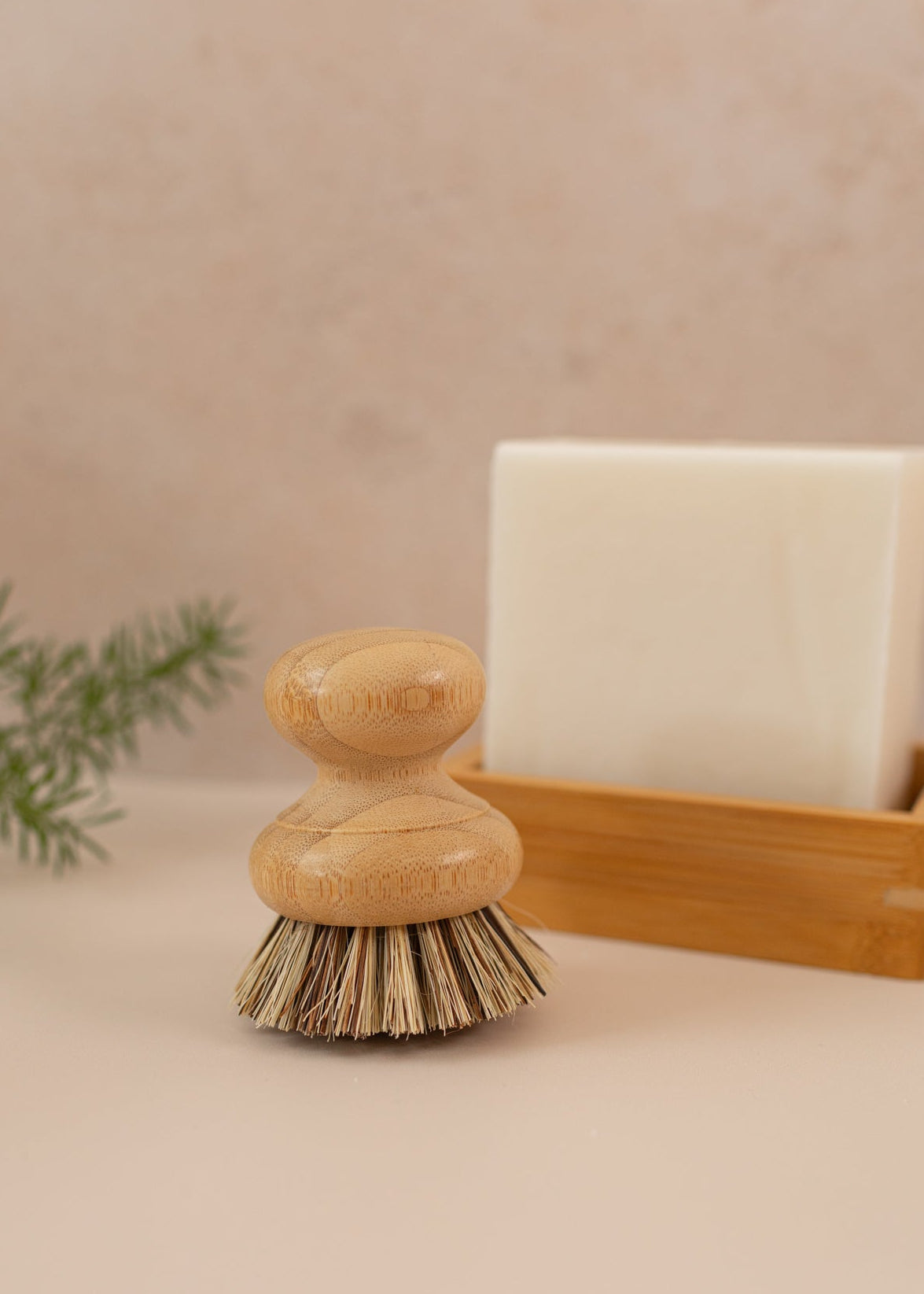 A dish brush on a pink backdrop with a dish block in the background