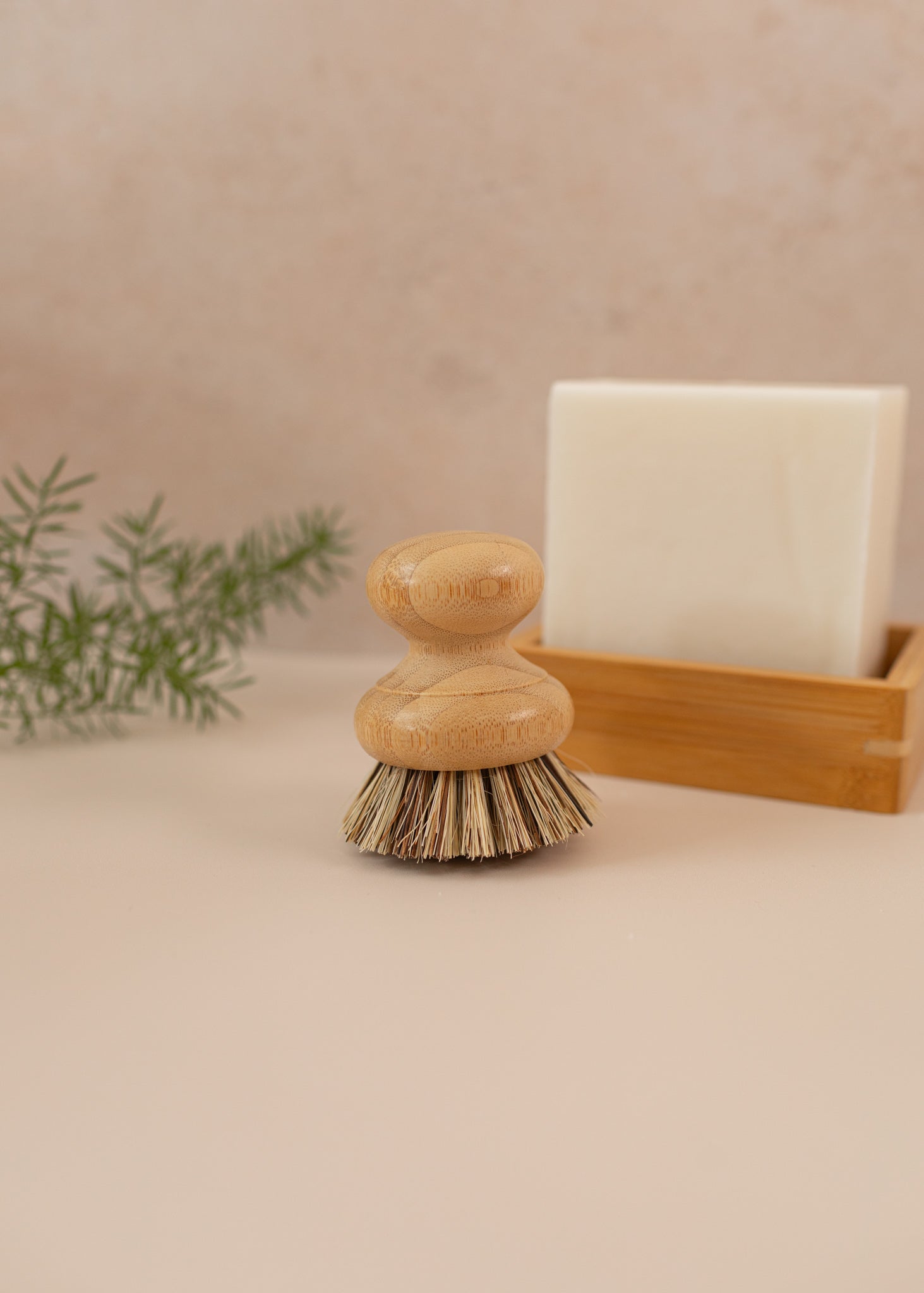 A dish brush on a pink backdrop with a dish block in the background