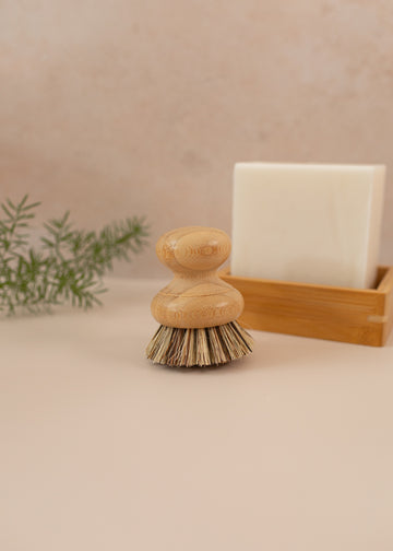 A dish brush on a pink backdrop with a dish block in the background