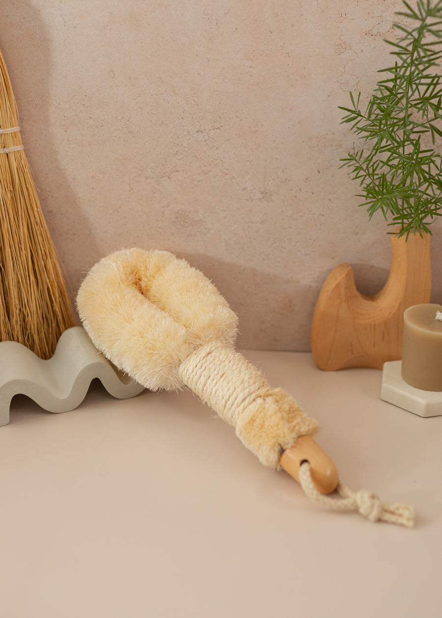 Dry brush propped up on a prop with rope around the handle. On a light pink backdrop
