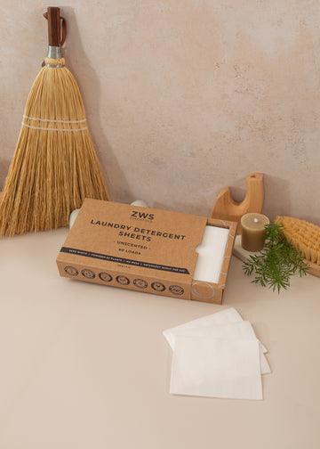 Laundry detergent sheets laid out on a light pink background with earthy props surrounding.
