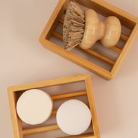 Two sustainable bamboo soap shelves, one with shampoo and conditioner bars, and one with a dish scrubber