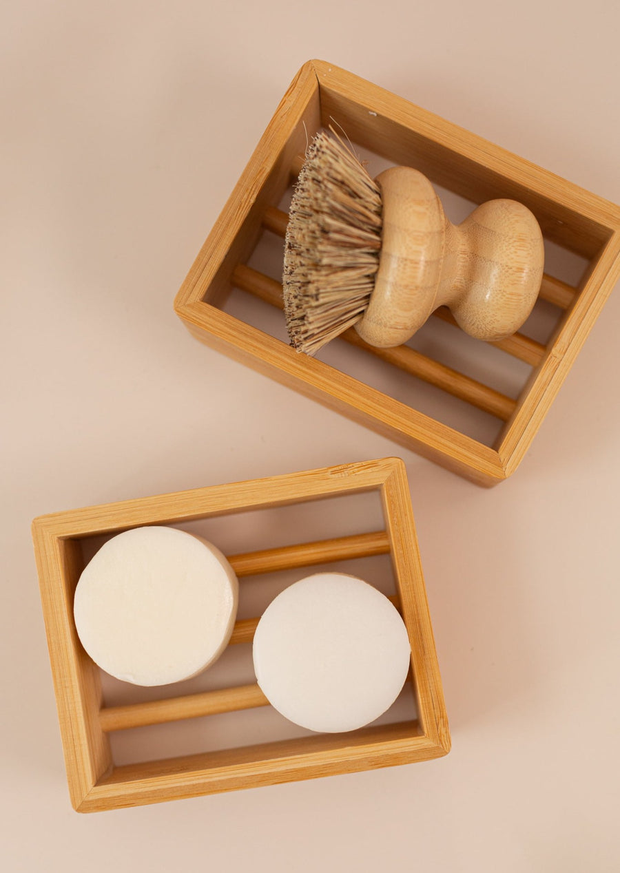 Two sustainable bamboo soap shelves, one with shampoo and conditioner bars, and one with a dish scrubber