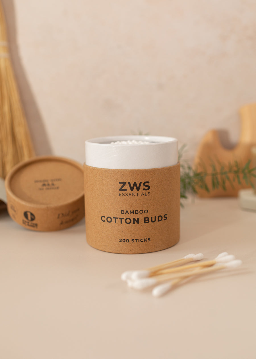 Rounded box of zero-waste cotton swabs by ZWS Essentials. Standing on a light pink background and a few cotton swabs laid out in the foreground