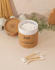 Rounded box of zero-waste cotton swabs by ZWS Essentials. Standing on a light pink background and a few cotton swabs laid out in the foreground