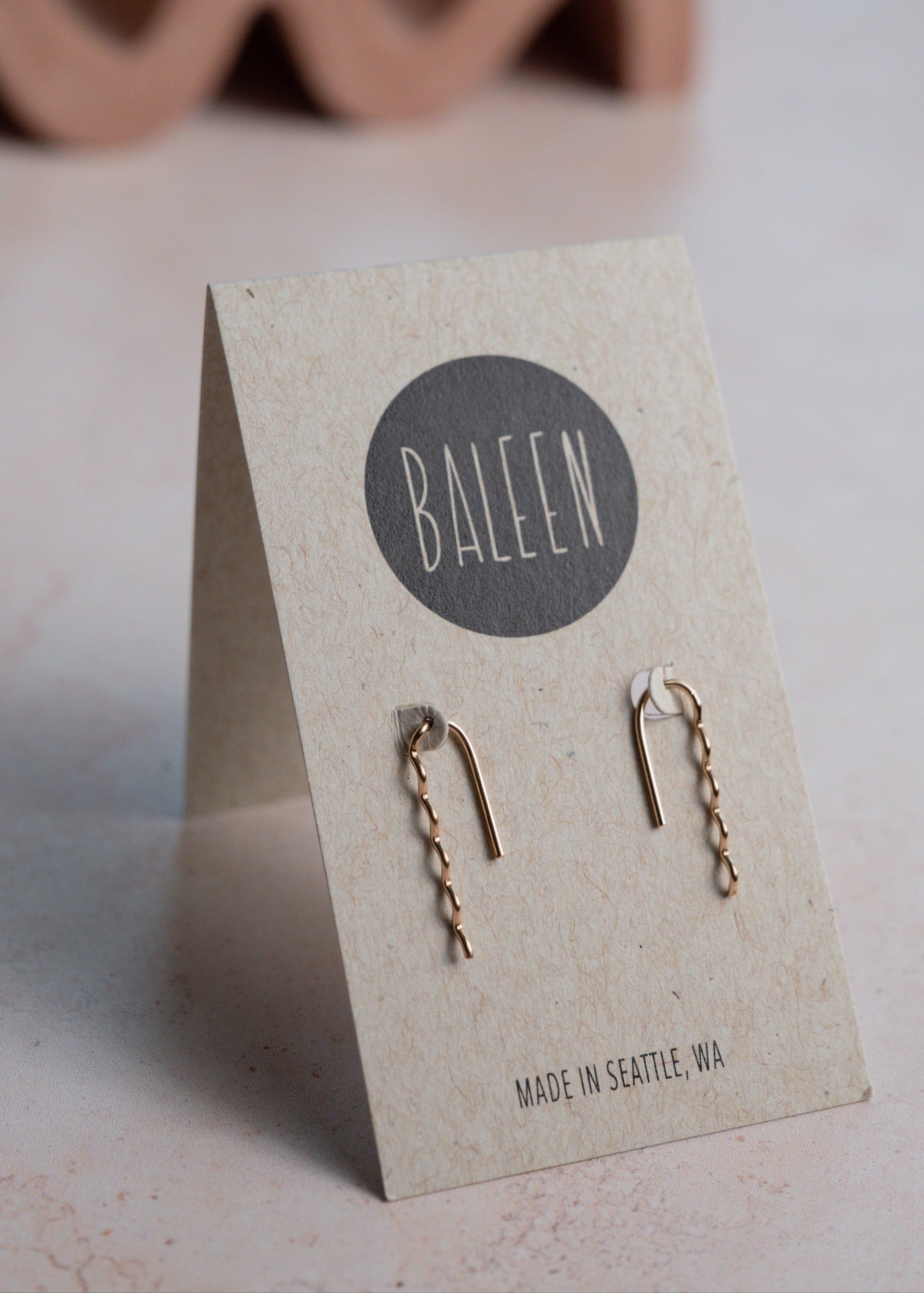 Gold earrings on a BALEEN branded card with a wavy object in the background