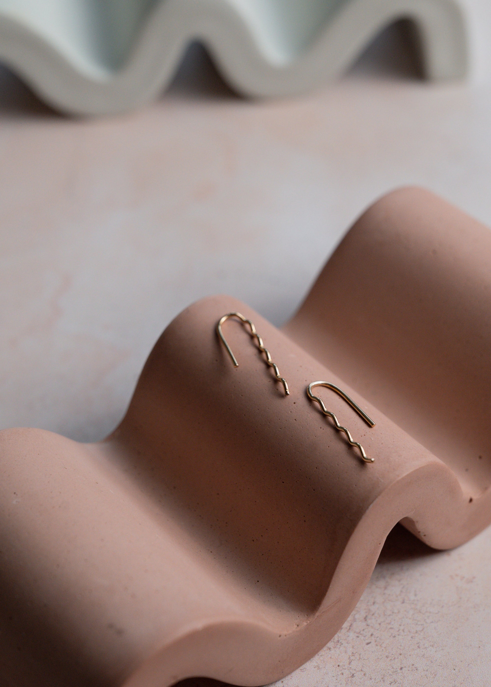 Gold earrings on a wavy pink jewelry stand with a blurred background