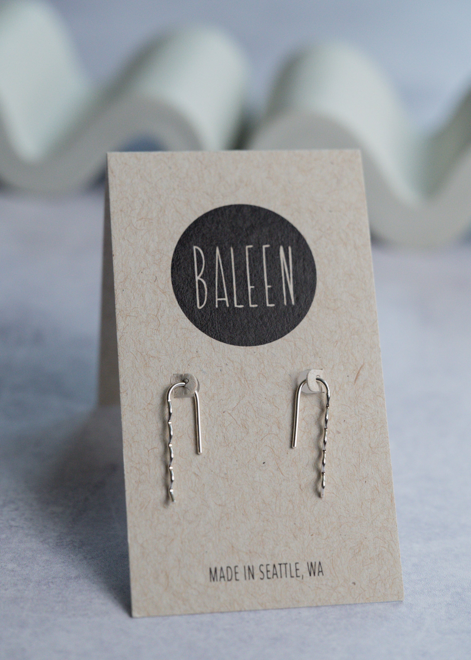 Pair of silver earrings on a 'BALEEN' branded card with a wavy background