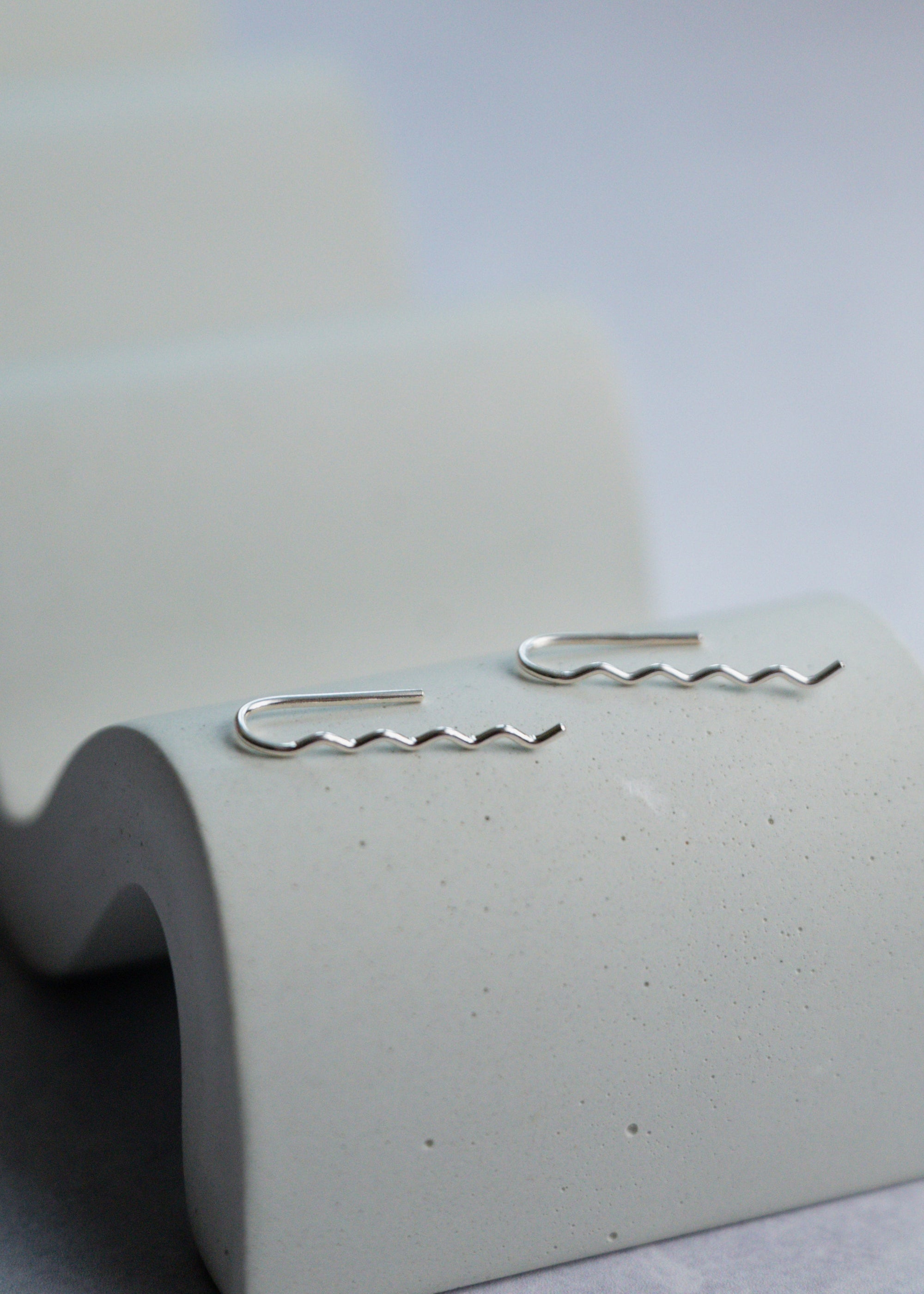 Silver wavy earrings on a textured white stand with a light gray background
