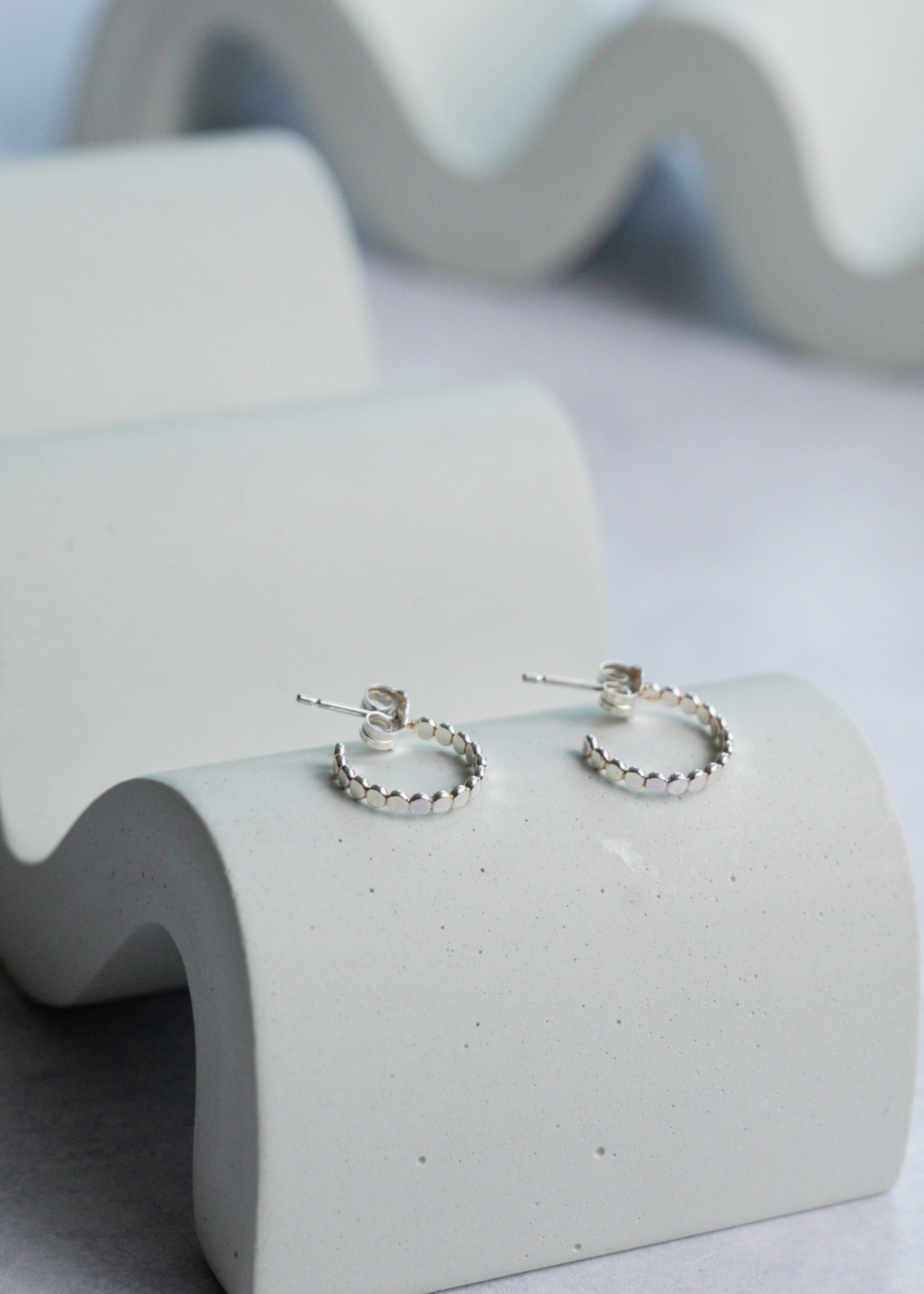 Silver hoop earrings on a concrete surface with a wavy background