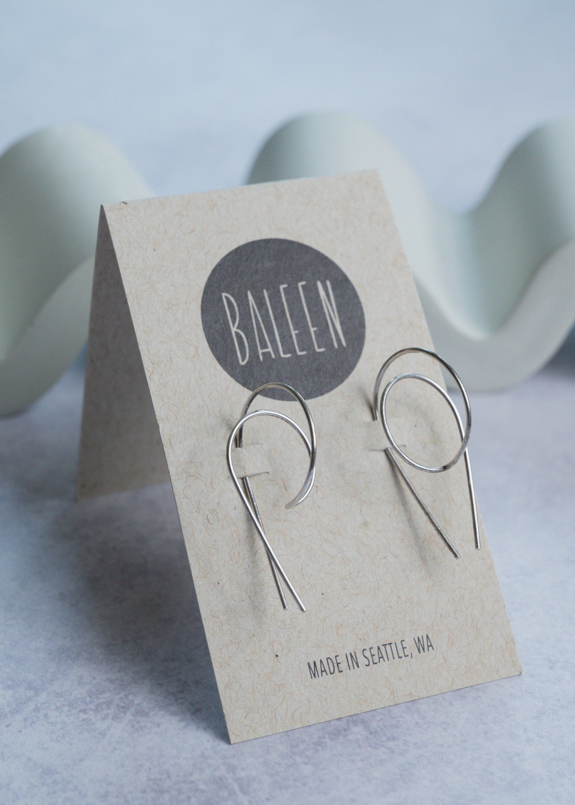Silver earrings on a 'BALEEN' branded card with a light background