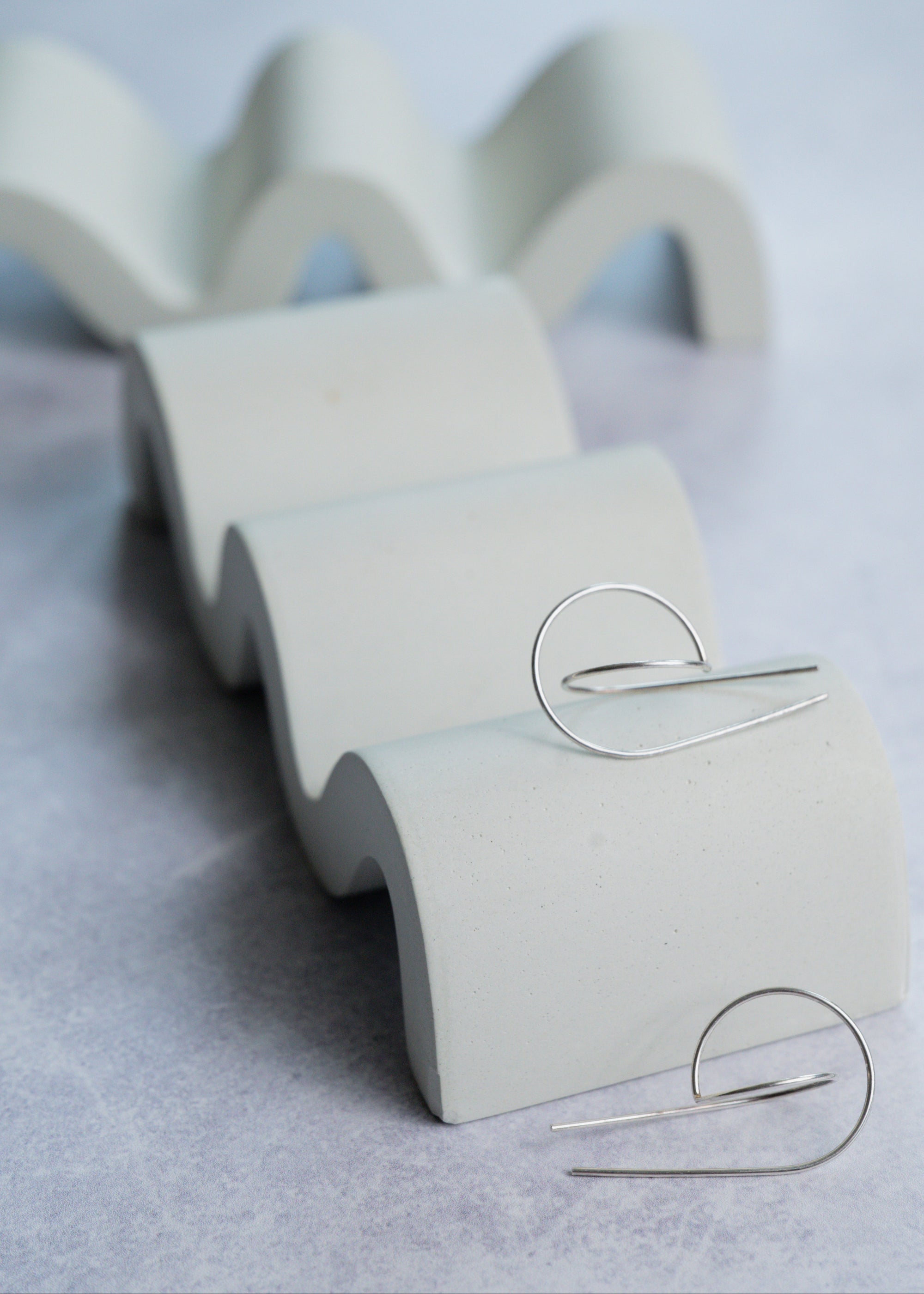 Silver sculpted hoops on a wavy stand against a light gray background