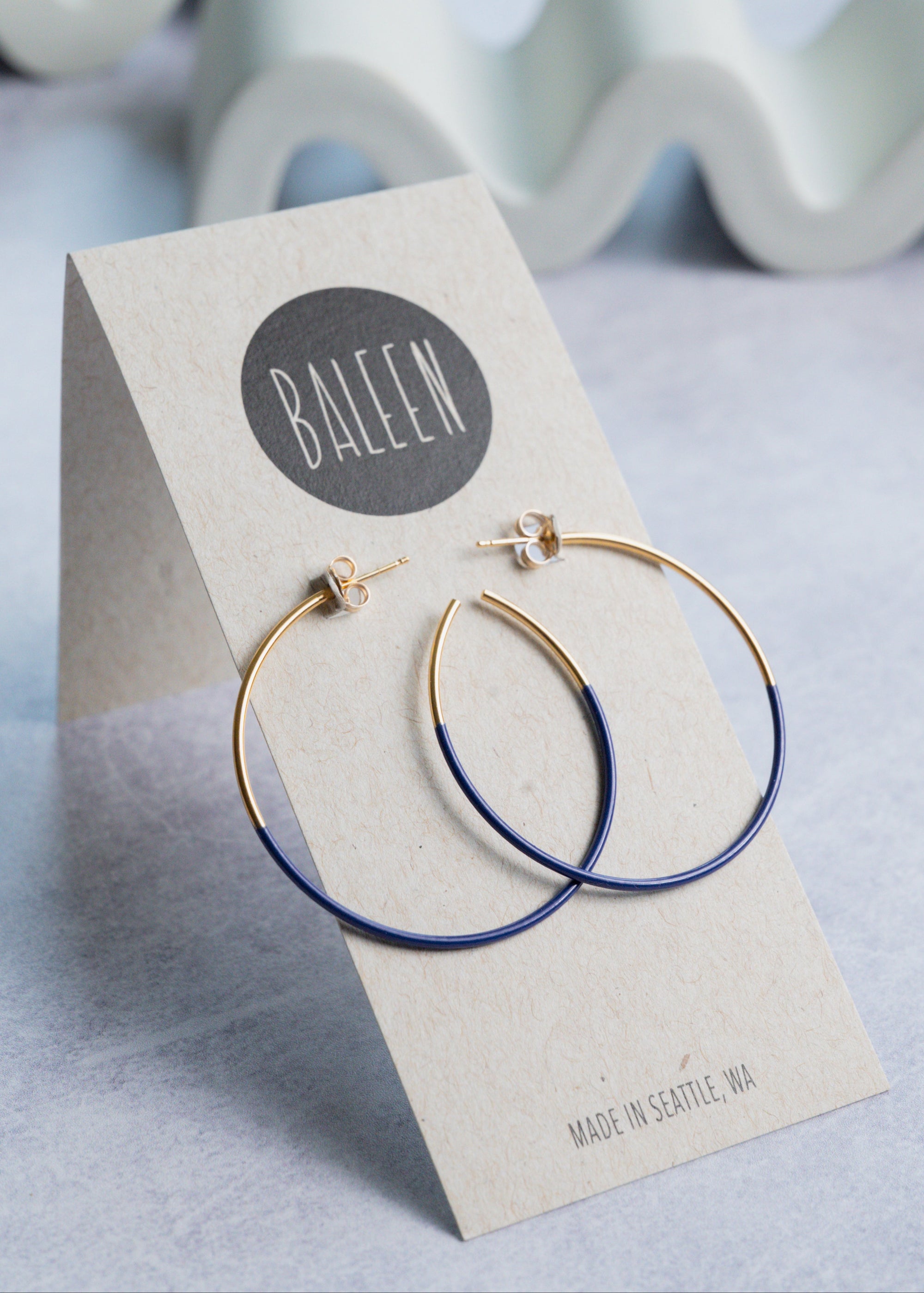 Gold and blue hoop earrings on a 'BALEEN' branded card
