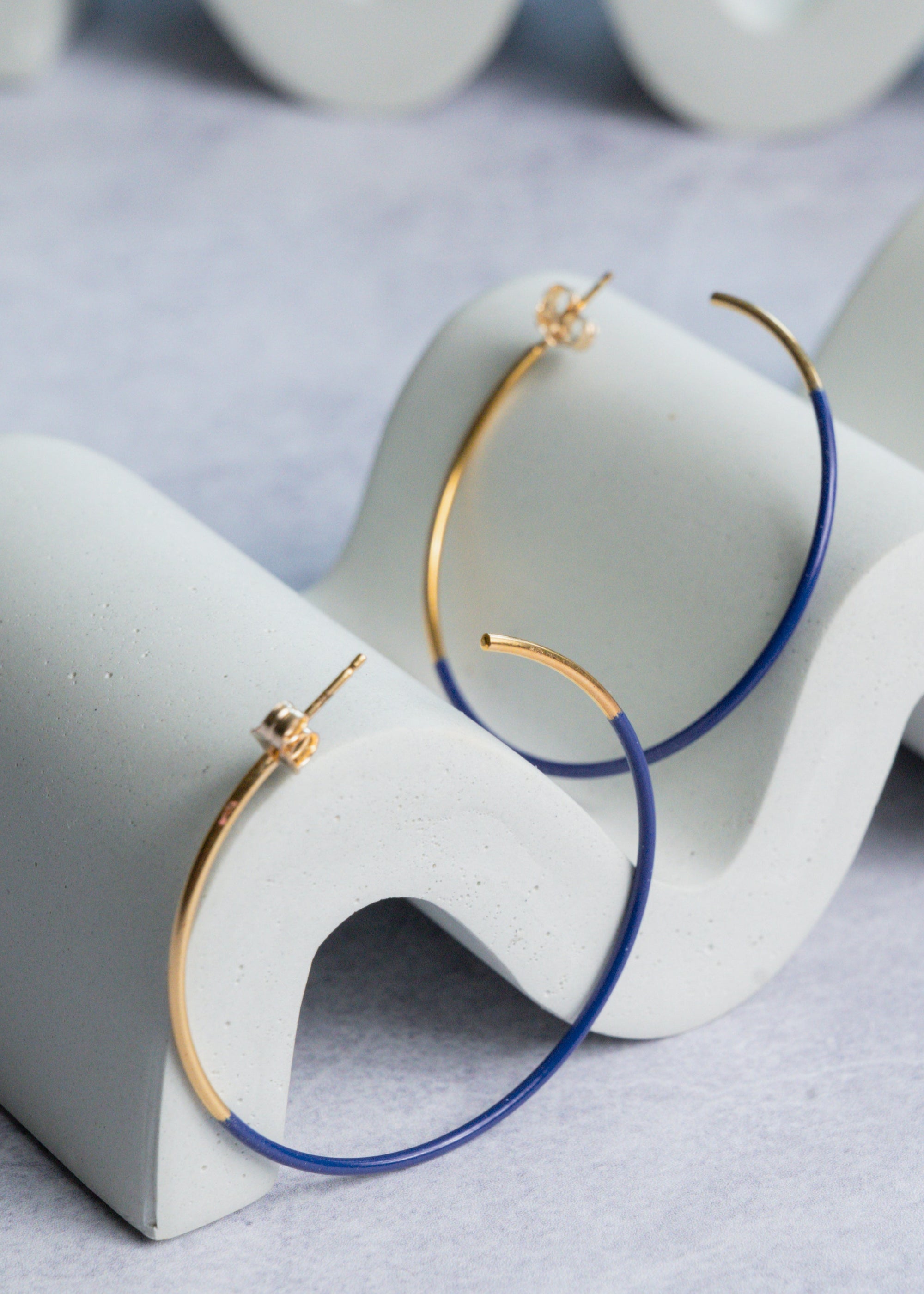 Gold and cobalt blue hoop earrings on a white stand