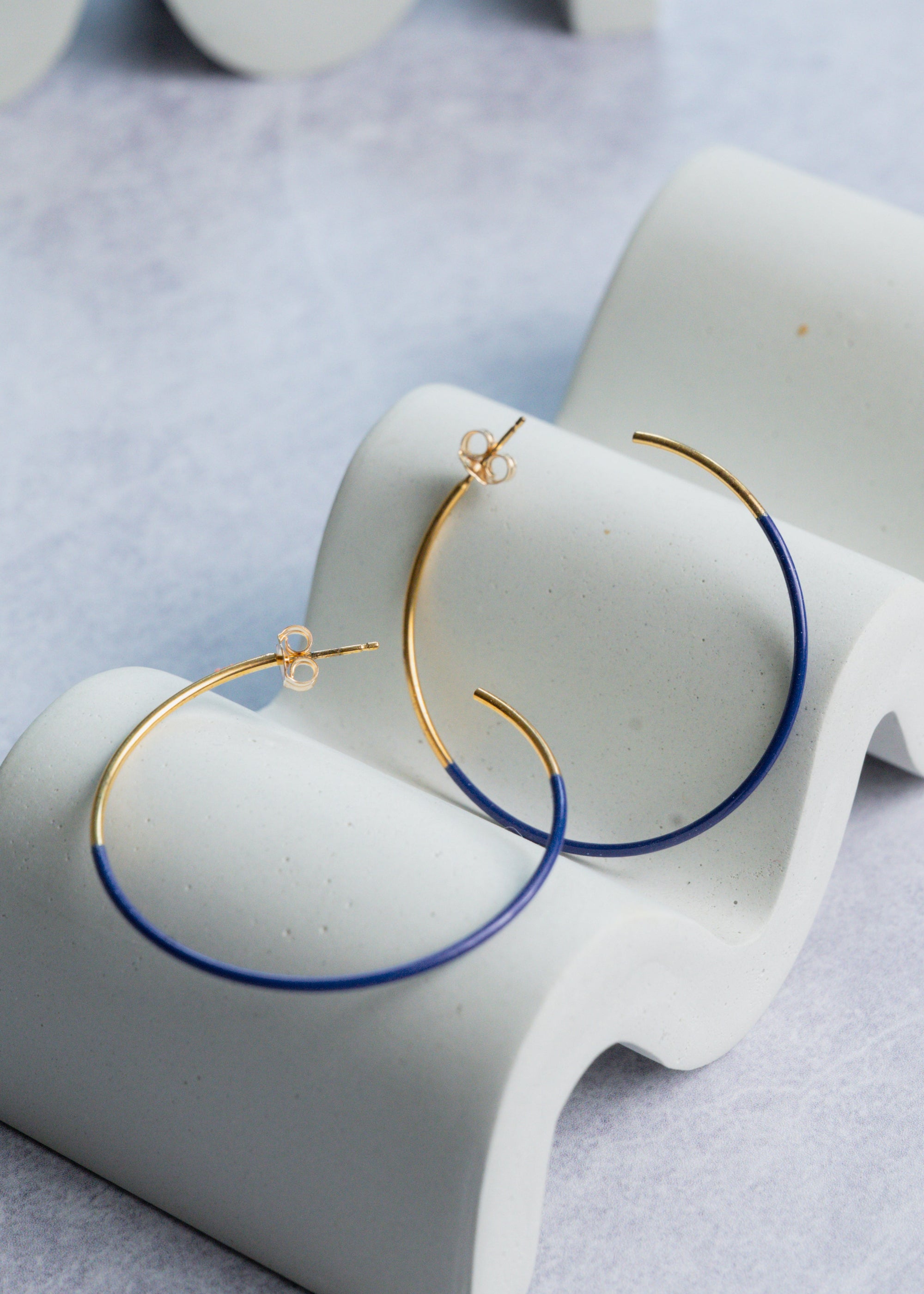 Gold and blue hoop earrings on a white stand with a light gray background