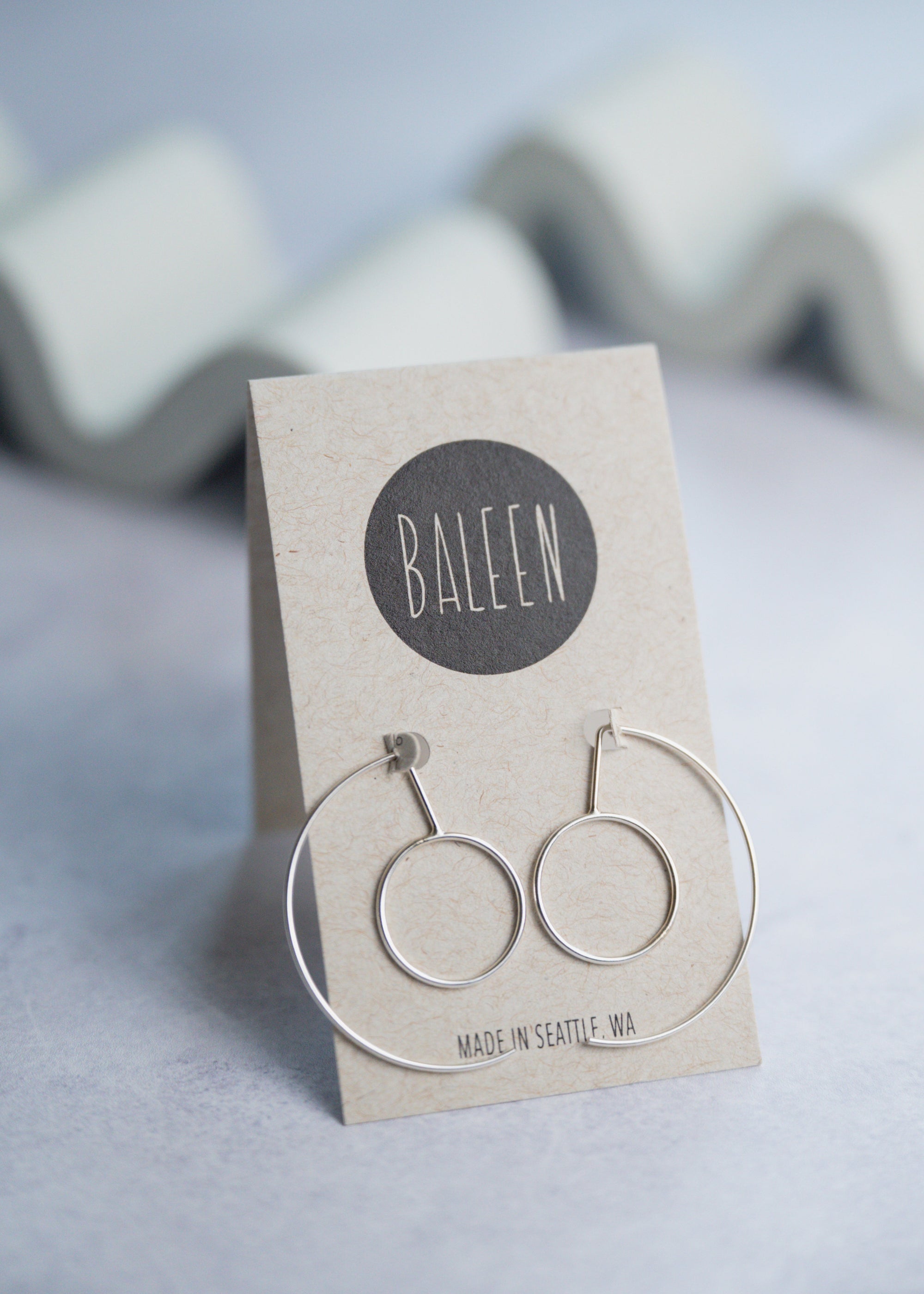 Baleen silver hoop earrings on a branded card with a gray background
