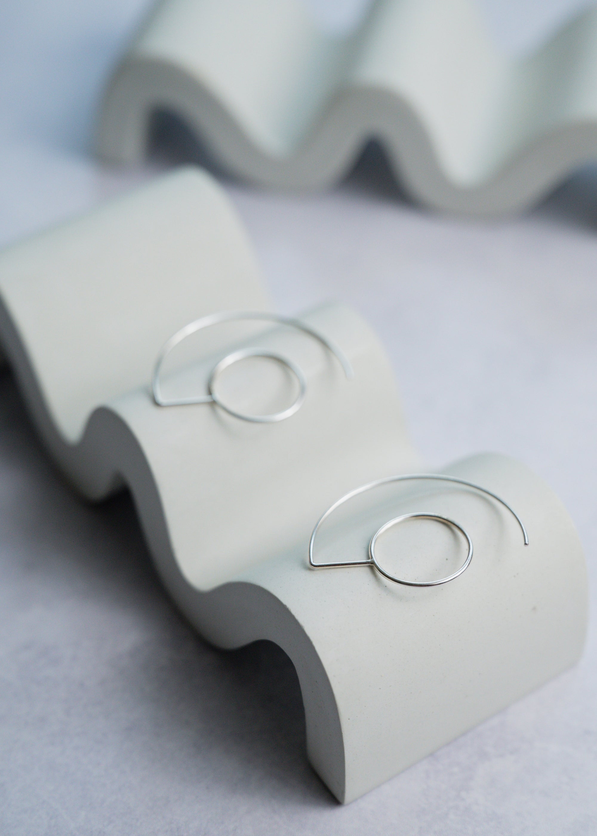 Silver earrings with circular designs on a  stand against a light gray background