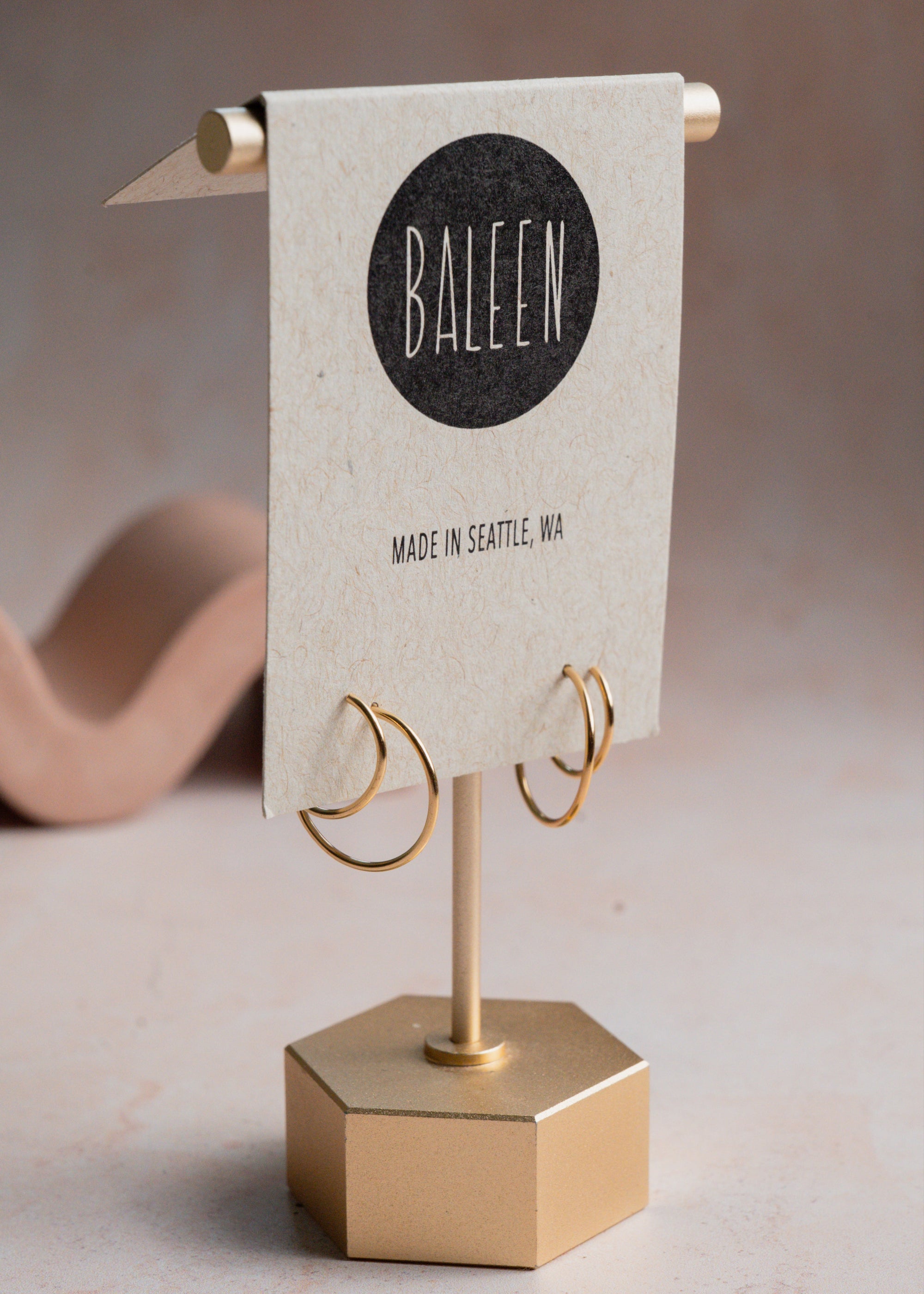 Gold double hoop earring on a stand with 'Baleen' branded card on a neutral background