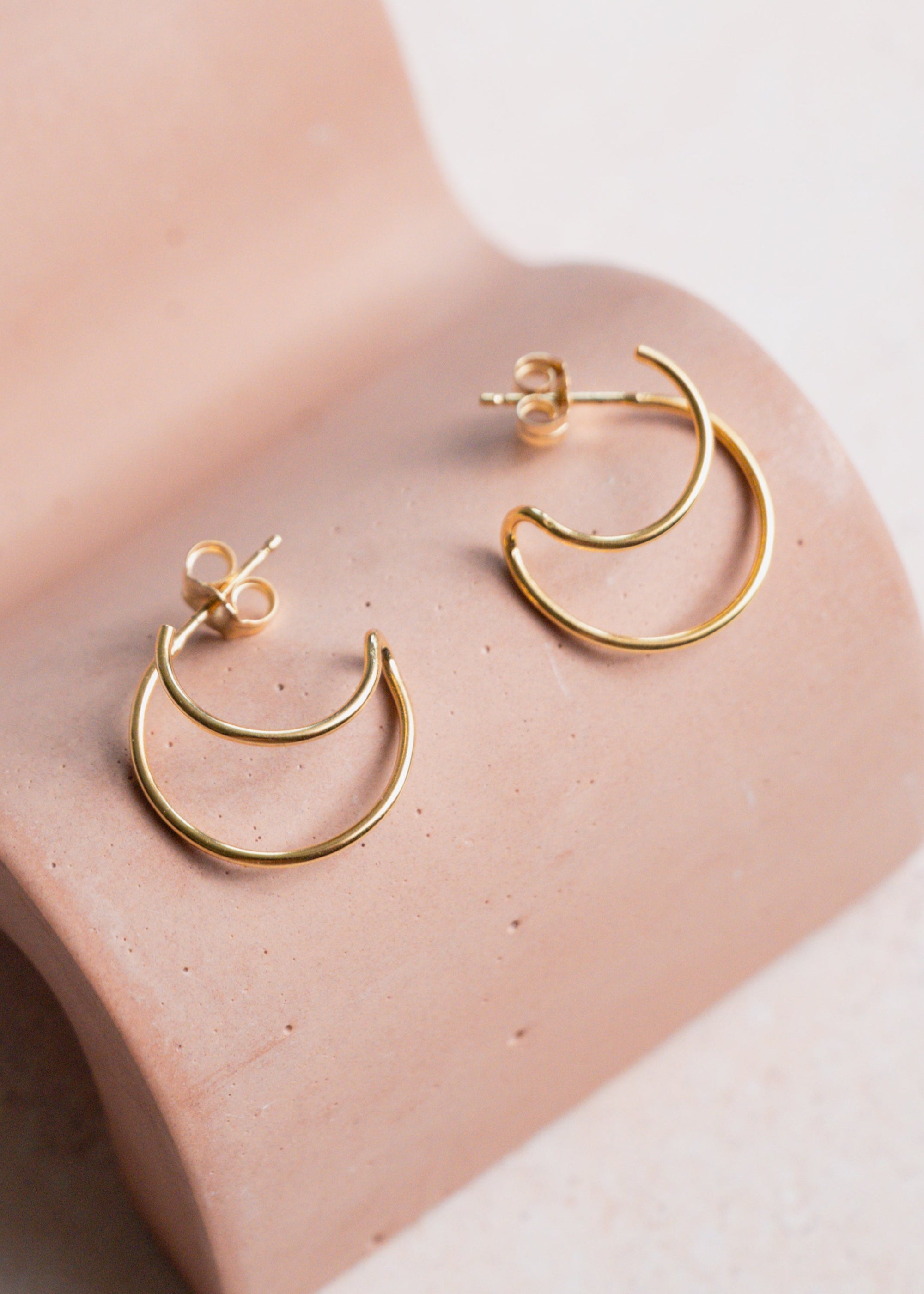 Gold hoop earrings on a pink concrete display against a neutral background
