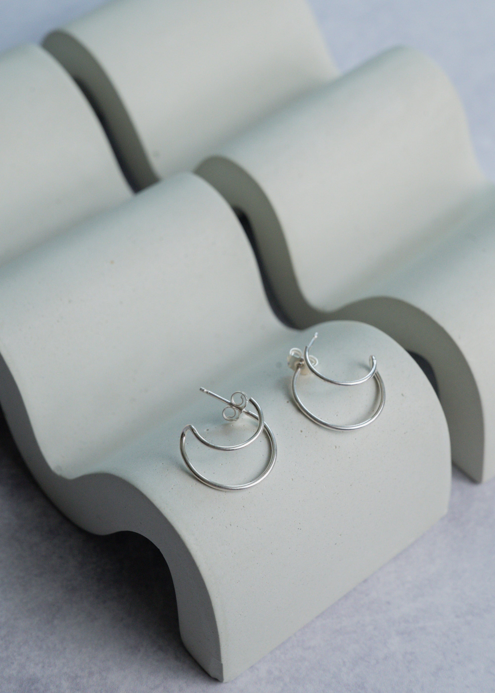 Silver hoop earrings on a concrete jewelry display against a light gray background