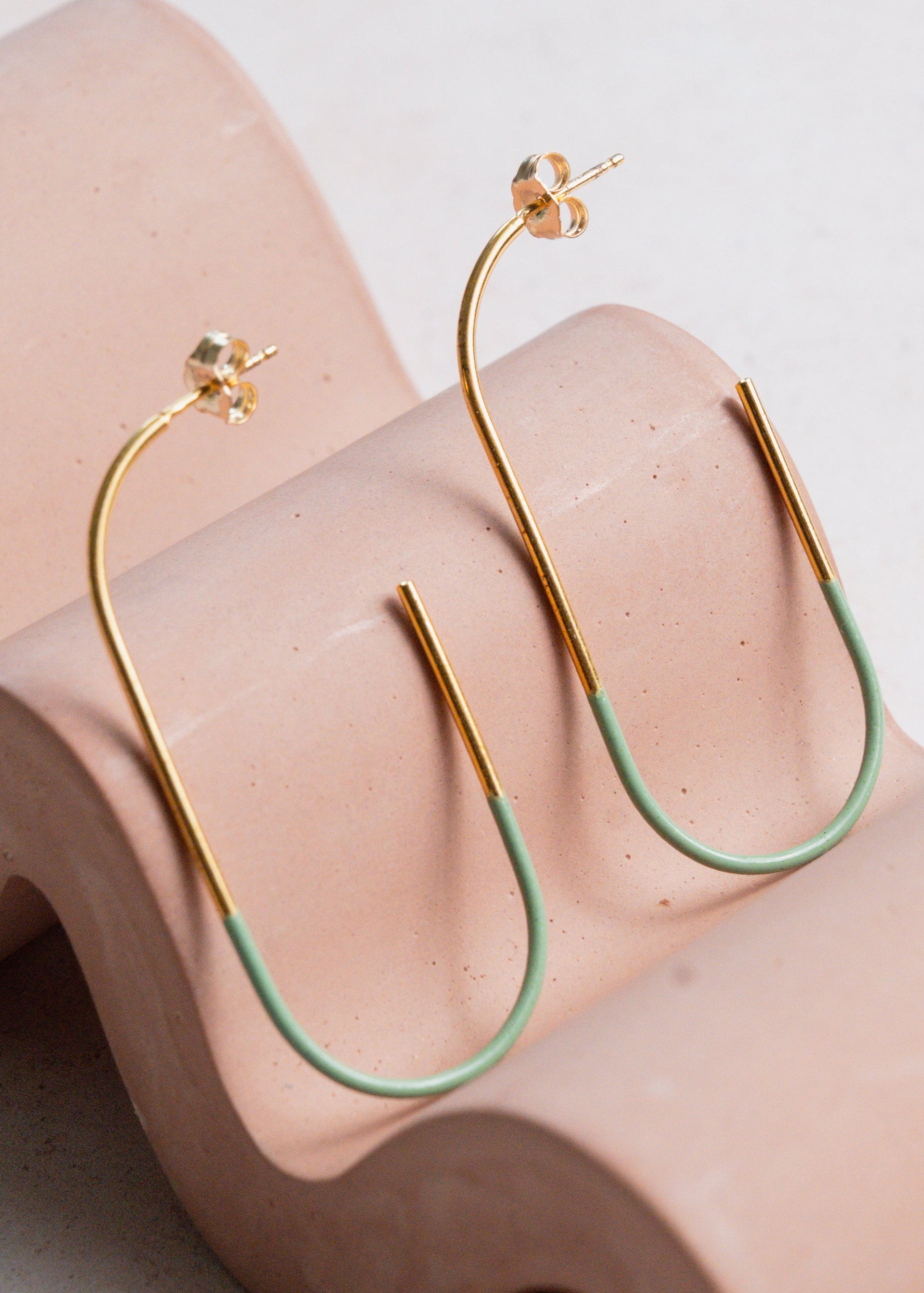 Gold and green hoop earrings on a wavy pink surface
