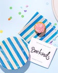 light blue background with two besswax covers, one folded up like a napkil with a cupcake on top and one covering a bwol, with confetti sprinkled around