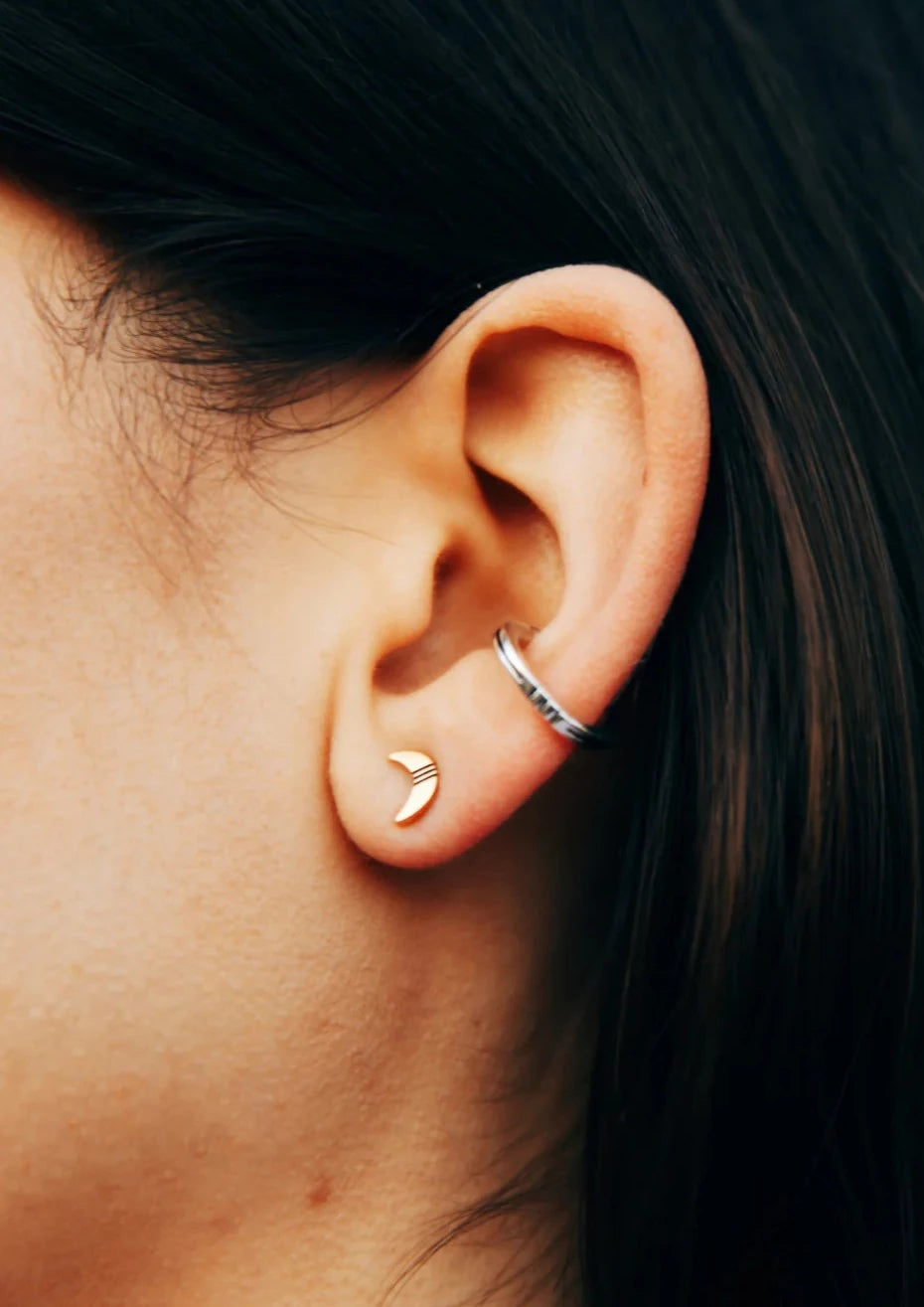 close-up of a models ear with a gold vermeil crescent moon stud, and just above it lies a silver cuff earring.