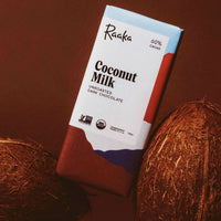 photo of the coconut milk chocolate bar leaning against two coconuts with a brown background